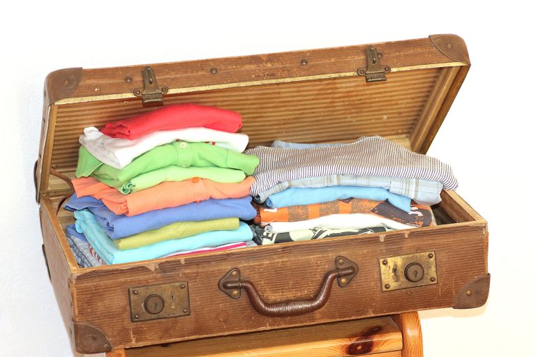 Ein aufgeklappter antiker Koffer ist mit bunter Kleidung gefüllt.