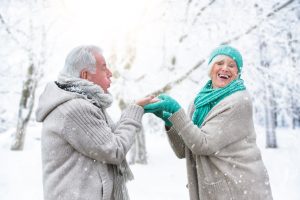 Ein älteres Paar amüsiert sich unter Schneeflocken in einer Winterlandschaft.