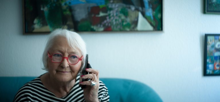 Ältere Dame am Telefon mit Silbernetz am Ohr.
