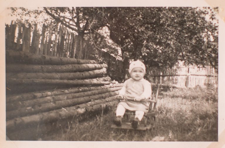 Die kleine Rosi sitzt vor einer Holzbank draußen im Garten.