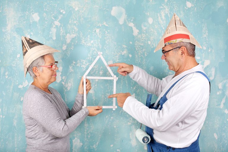 Älteres Ehepaar lacht sich an beim Renovieren und hat Zollstock als Haus geformt in der Hand.