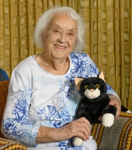 Eine Seniorin sitzt im Sessel und streichelt glücklich eine Stoffkatze.