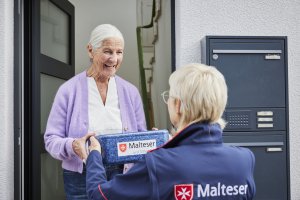 Malteser Mitarbeiter bringt Essen zu Seniorin.