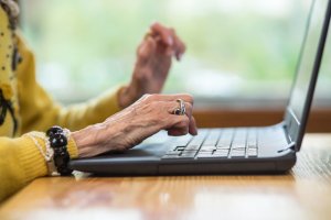 Hände einer Senioren liegen auf der Tastatur eines Laptops.