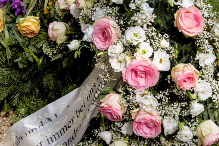Welke Blumen mit Erinnerungsschriftzug liegen auf einem Grab.