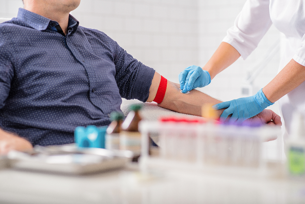 Mann sitzt beim Blutspenden mit abgebundenem Arm für das Einstechen der Nadel.