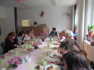 Eine Gruppe älterer Menschen sitzt an einer Tafel, isst und kommuniziert. In der Mitte stehen kleine Blumengestecke. Foto: MGH Bernsdorf